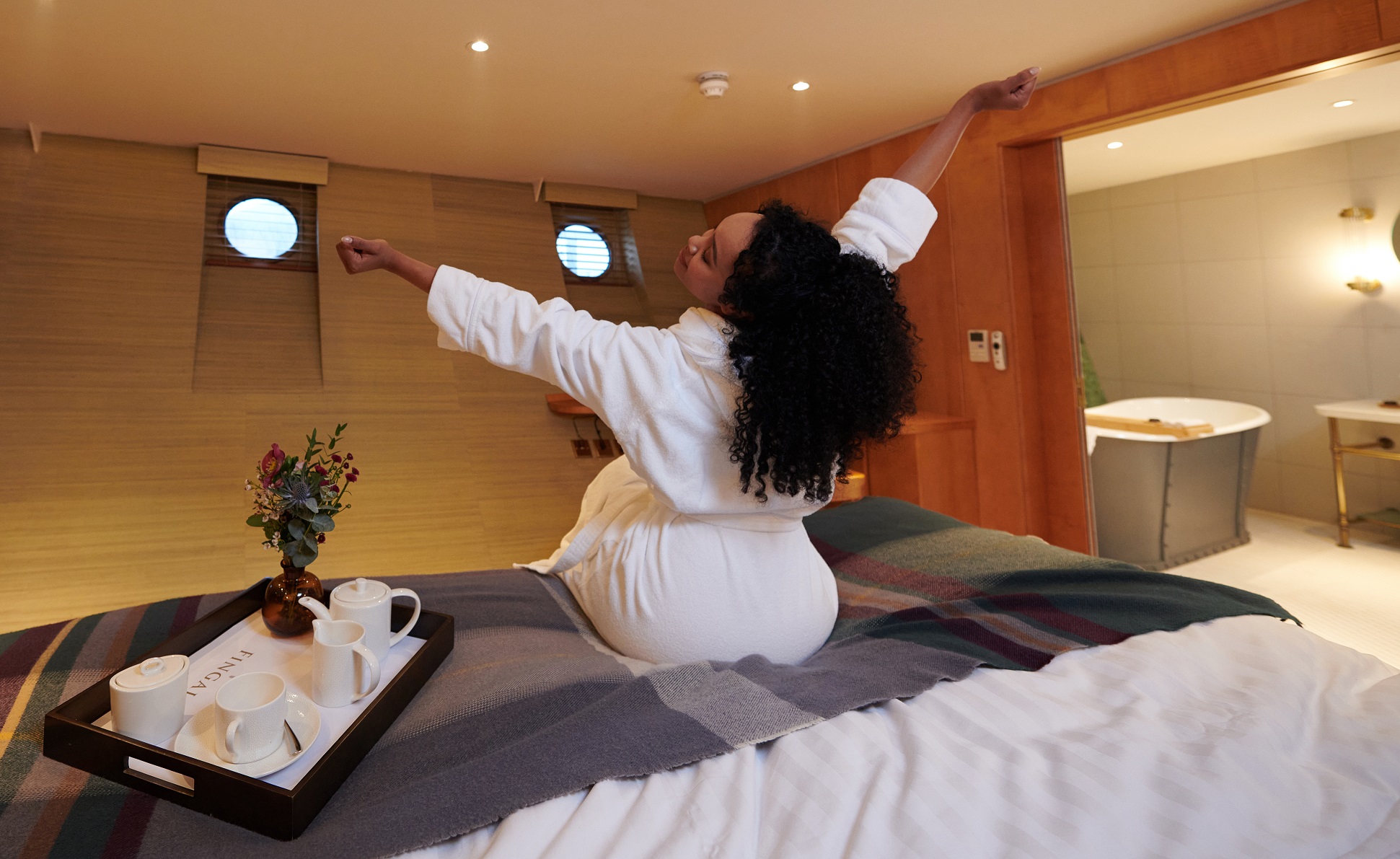 Women stretching arms while sitting on a bed. 